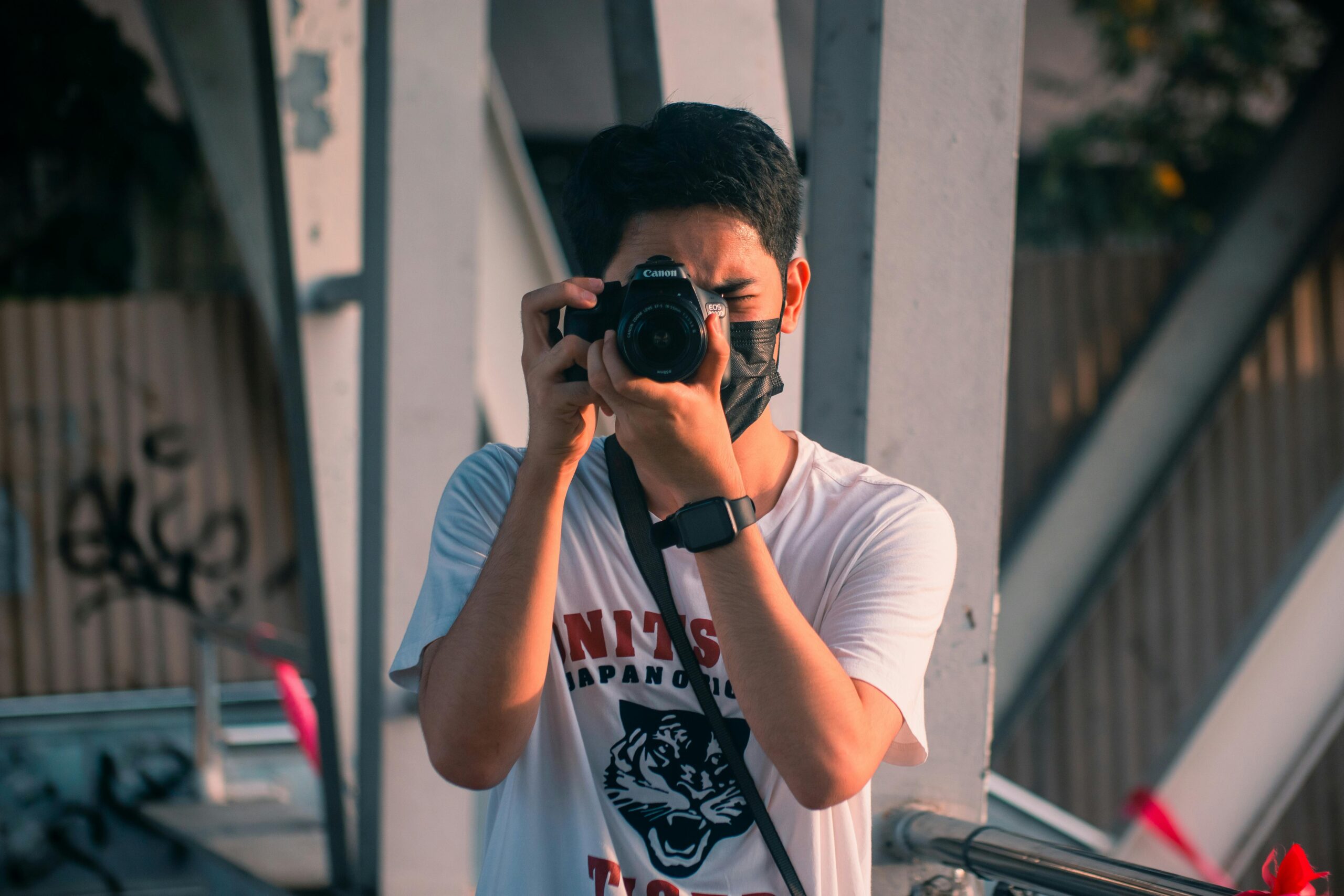 Photographer wearing a face mask captures an outdoor scene with a DSLR camera.