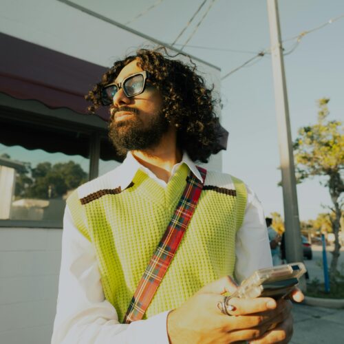 A fashionable man with curly hair and sunglasses enjoying the sunny street.